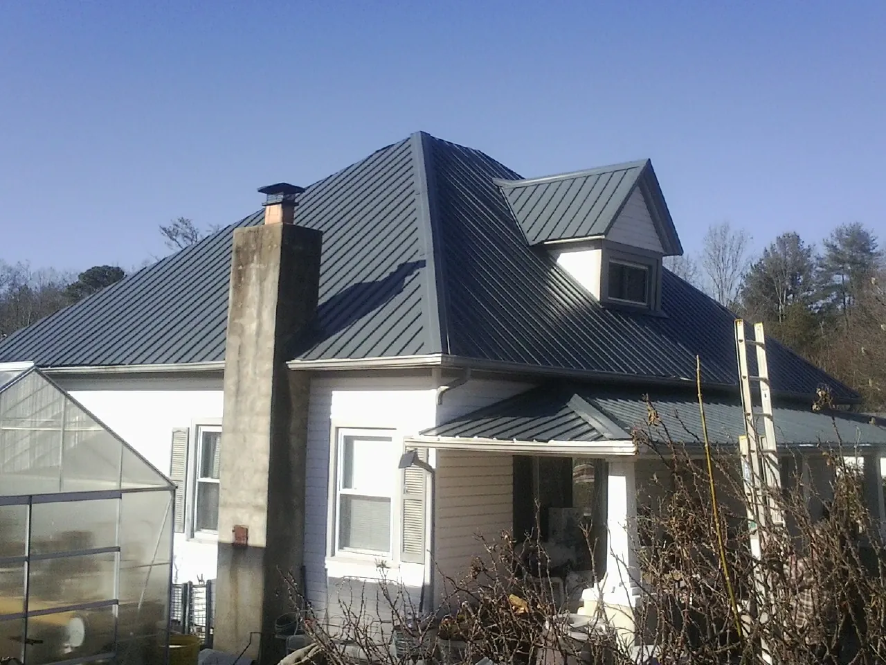 Dark blue standing seam metal roof on a white farmhouse with dormer — Slate & Tile Roof Repair by Roofing Brothers in Middleton