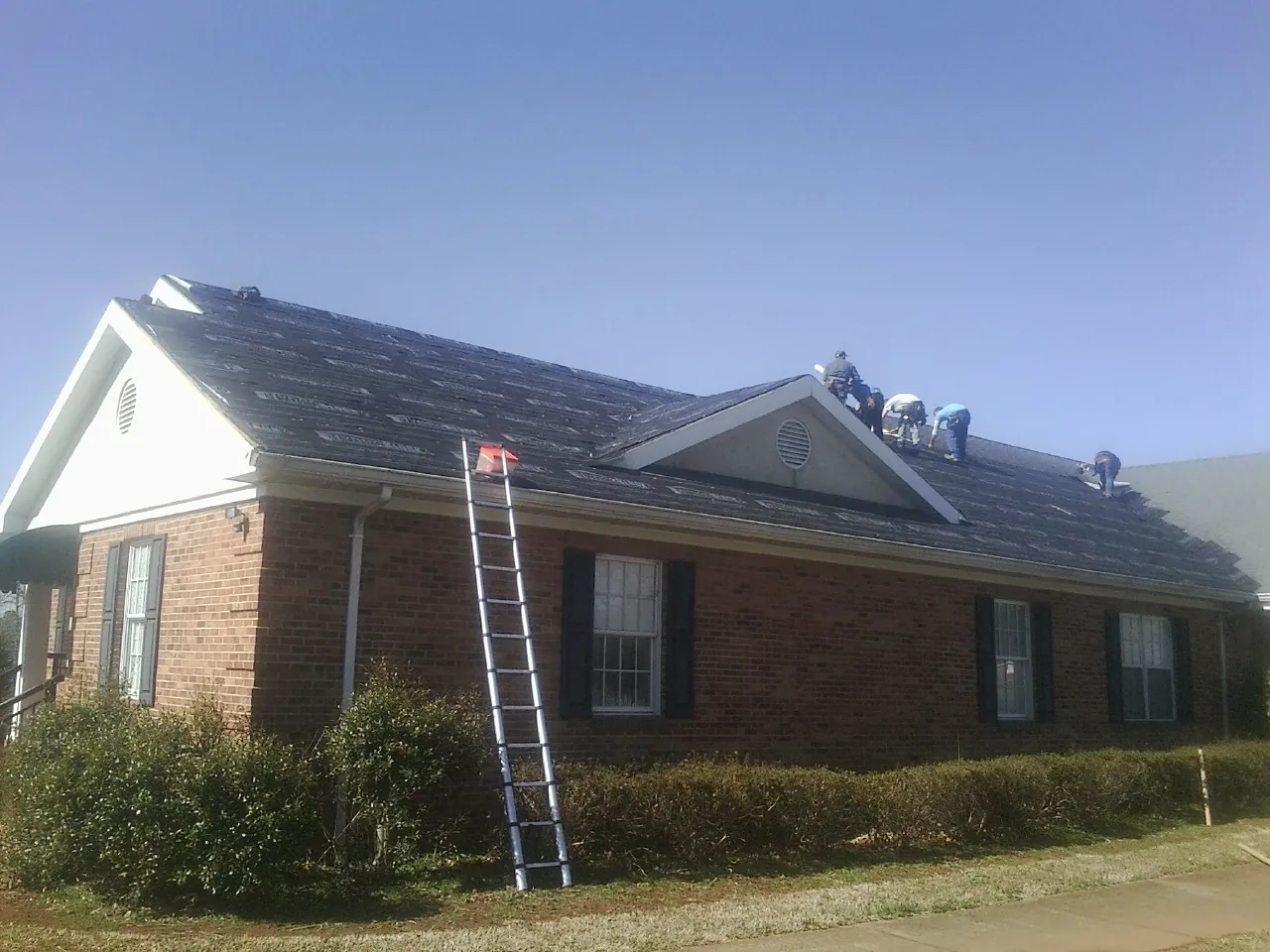 Crew tearing shingles off a brick ranch roof with a ladder set — Metal Roof Repair work by our crew in Middleton